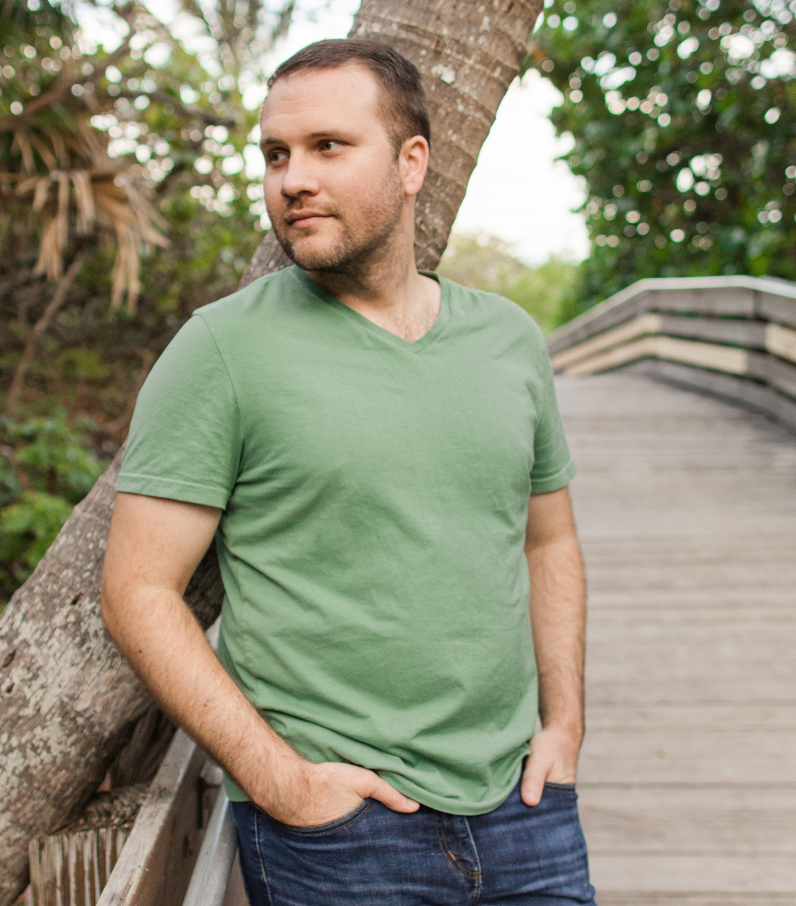 A 31-Year-Old American Man with Short Brown Hair & Green Eyes Dressed in Classic Green V-Neck T-Shirt & Navy Denim Jeans, Enjoying Nature on a Boardwalk in a Woodsy Forest in South Florida smiling women in white shirt and open hair