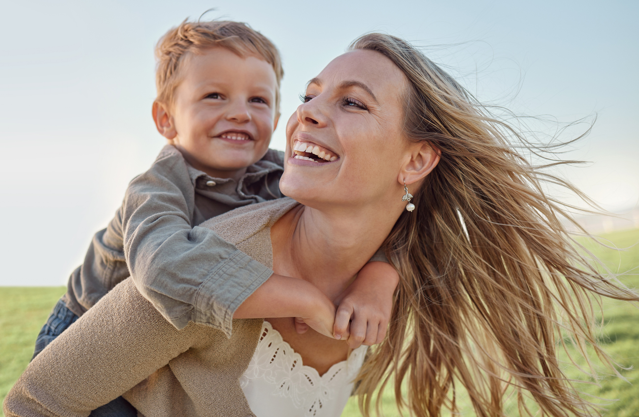 Mother, child and happy piggyback in summer, holiday and blue sky, sunshine and play in a green park. Happy mother, kid and smile having fun outdoor for vacation with smile, laugh and love in nature mom and daughter