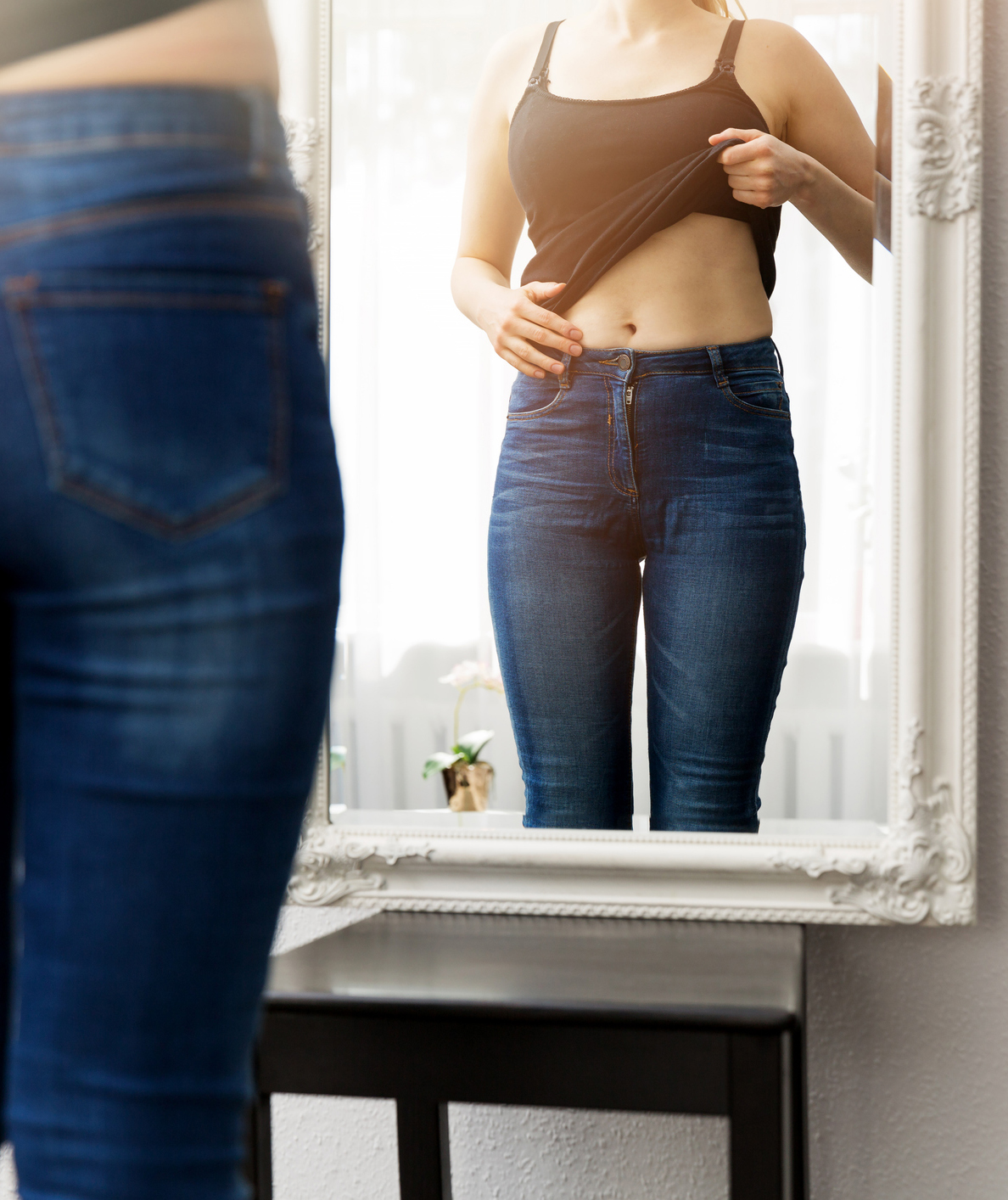 woman checking her body in front of mirror smiling women in white shirt and open hair